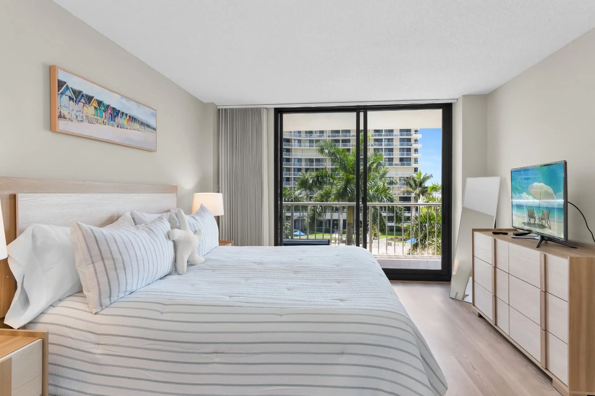 Primary bedroom with a large bed, coastal artwork and sliding doors to the balcony